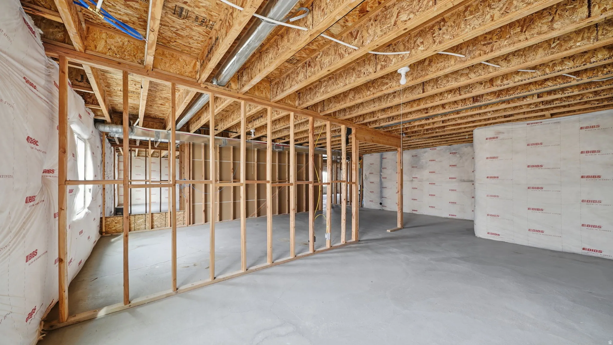 Unfinished basement with concrete flooring, exposed wooden joists, framed interior walls, and insulated exterior walls