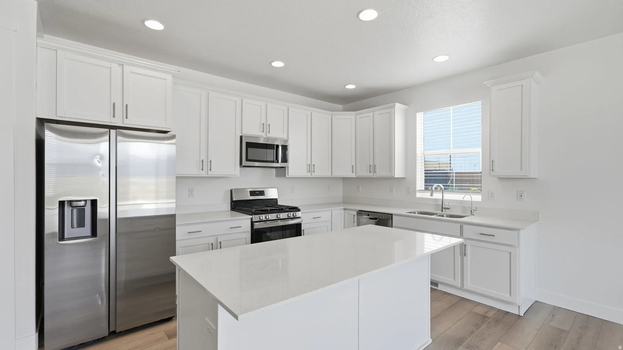 Well-appointed kitchen featuring white cabinetry, quartz counters, stainless steel appliances, a center island, recessed lighting, and wood-finish flooring