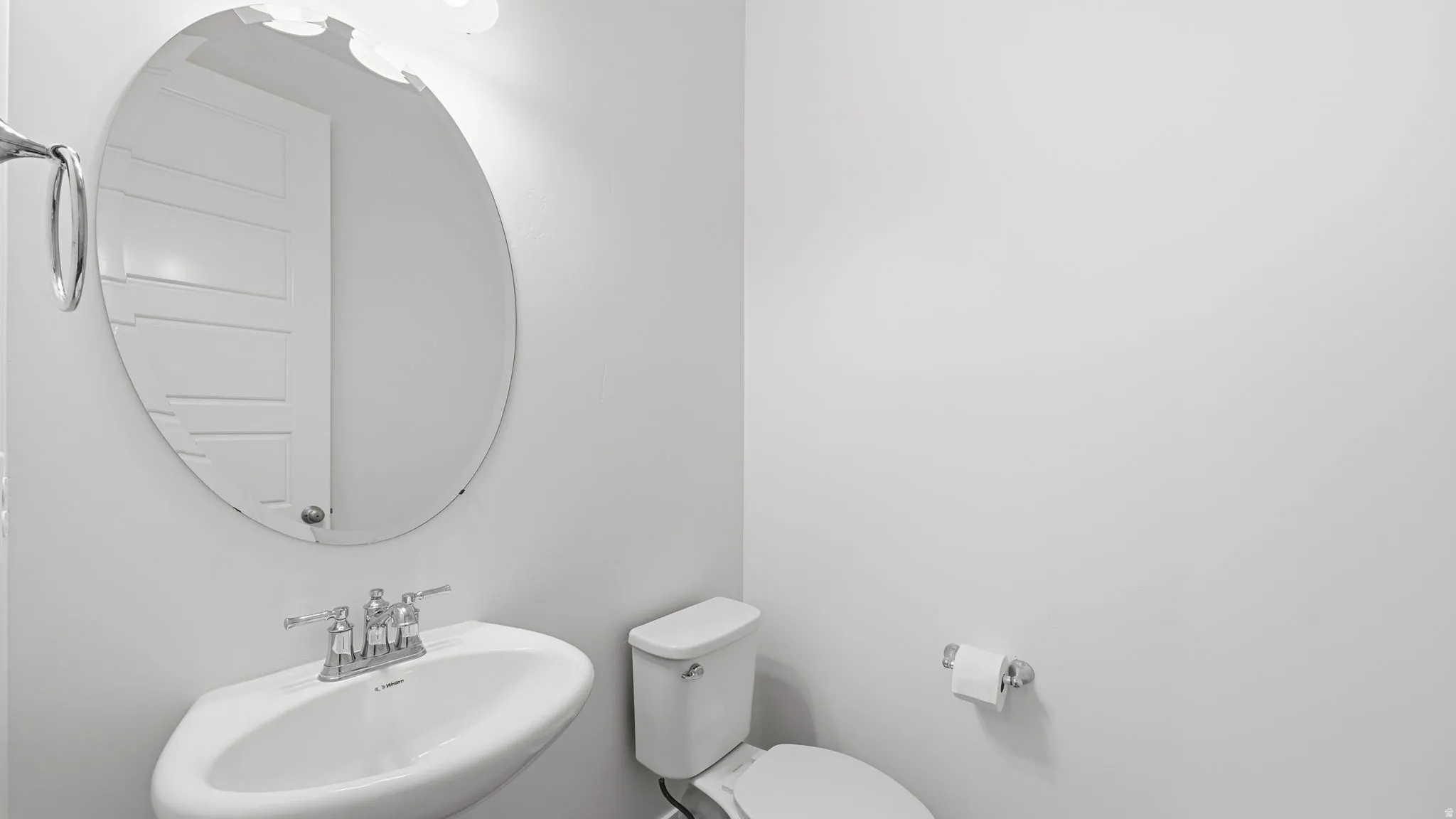 Pedestal sink with chrome faucet, oval mirror, wall-mounted light fixture, and white toilet, off mud room