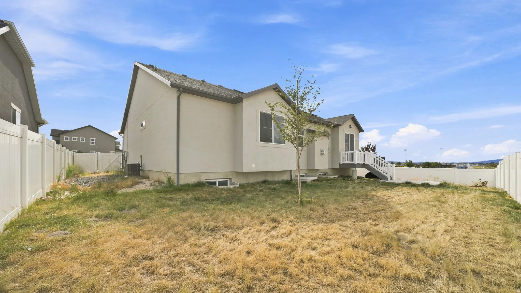 Expansive rear exterior with stucco siding, white vinyl fencing with double gate entry, and a raised deck with stairs