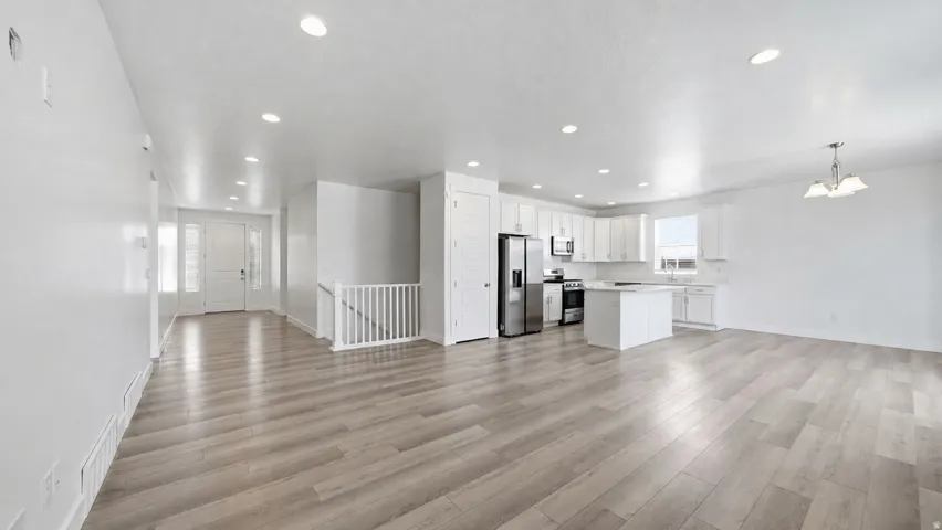 Open-concept living space with wood-finish flooring, recessed lighting, white cabinetry, a kitchen island, and stainless steel appliances