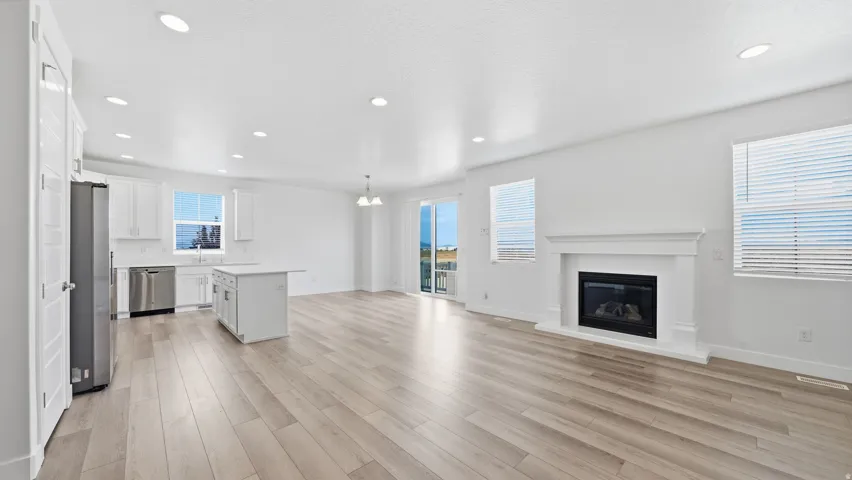 Open-concept living area featuring wood-finish flooring, a white kitchen island, stainless steel appliances, a white mantel fireplace, and recessed lighting