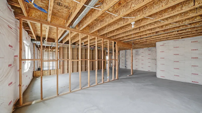 Unfinished basement with concrete flooring, exposed wooden joists, framed interior walls, and insulated exterior walls