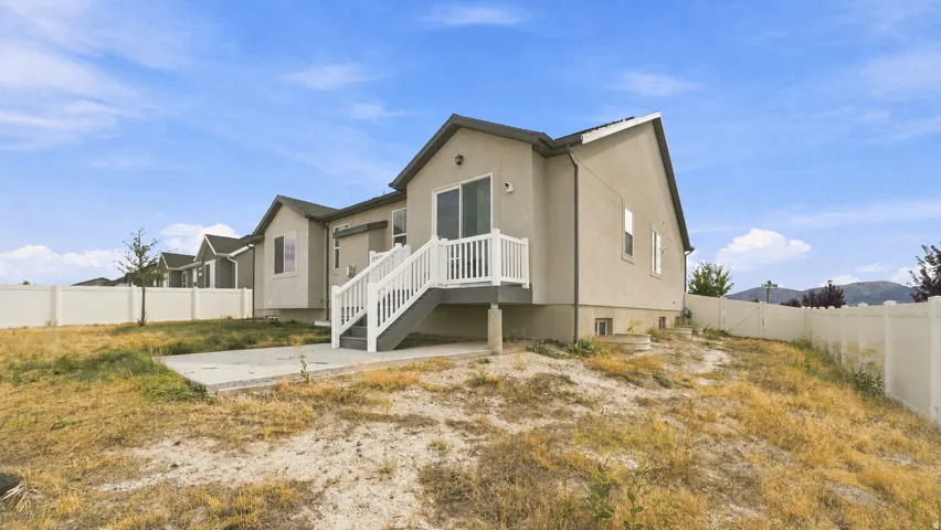 Exterior featuring light-toned stucco siding, white vinyl fencing, and a concrete patio