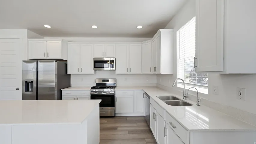 White shaker cabinetry, stainless steel appliances, light-toned countertops, wood-finish flooring, and recessed lighting