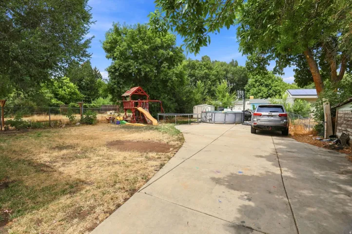 Paved driveway leading to a private outdoor area, featuring mature trees and partial fencing