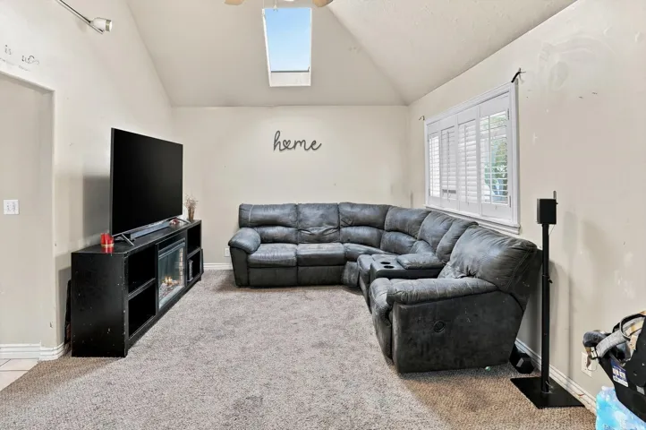 Vaulted ceiling with a skylight, window with plantation shutters, and a built-in media console with an electric fireplace