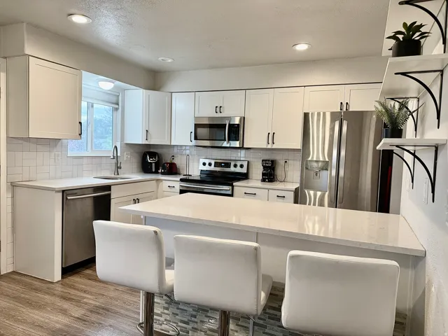 Contemporary kitchen featuring white cabinetry, stainless steel appliances, light countertops, a subway tile backsplash, and wood-finish flooring
