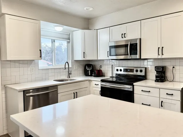 White shaker cabinetry, stainless steel appliances, quartz countertops, subway tile backsplash, and a kitchen island