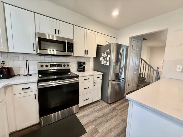 White shaker-style cabinetry, stainless steel appliances, light-toned countertops, subway tile backsplash, and wood-finish flooring