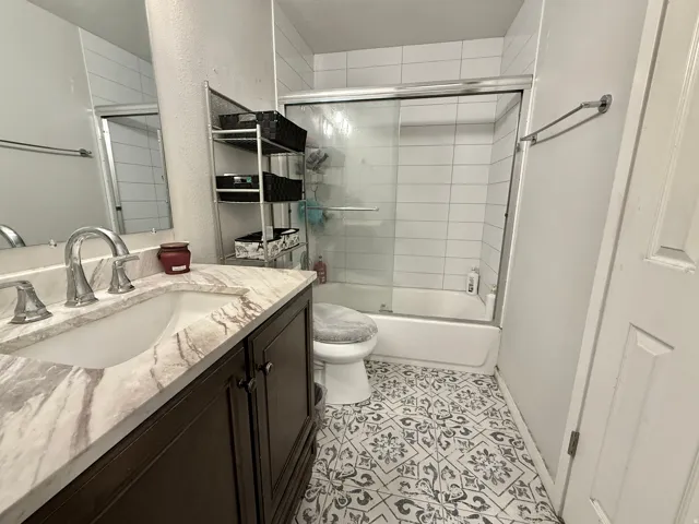 Bathroom featuring a vanity with an integrated sink, patterned floor tile, a bathtub with a sliding glass enclosure, and subway tile shower surround