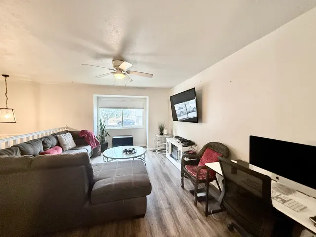 Living area featuring wood-finish flooring, a ceiling fan with integrated lighting, and a white railing