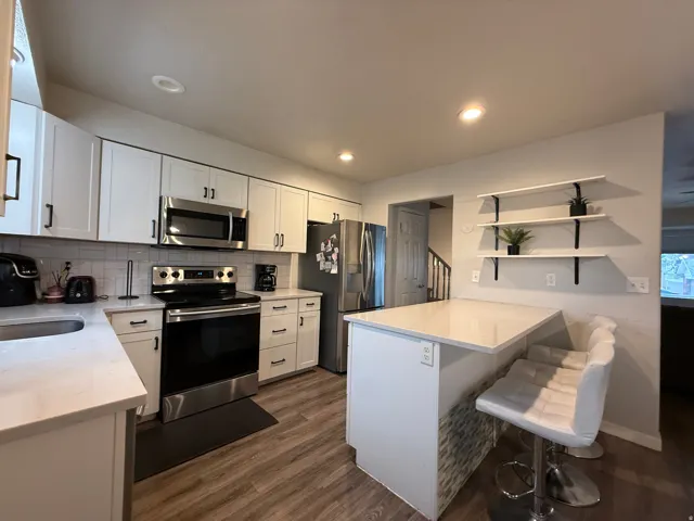 Kitchen featuring white cabinetry with black hardware, stainless steel appliances, a tiled backsplash, wood-finish flooring, and a breakfast bar with a stacked stone accent