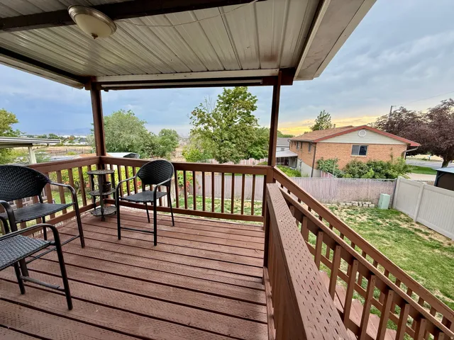 Expansive covered deck with brown wood-finish flooring and railings, featuring a fixed overhead light fixture and a green lawn below
