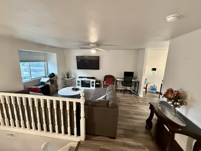 Open-concept living area featuring wood-finish flooring, a contemporary ceiling fan, and a built-in media console with a fireplace