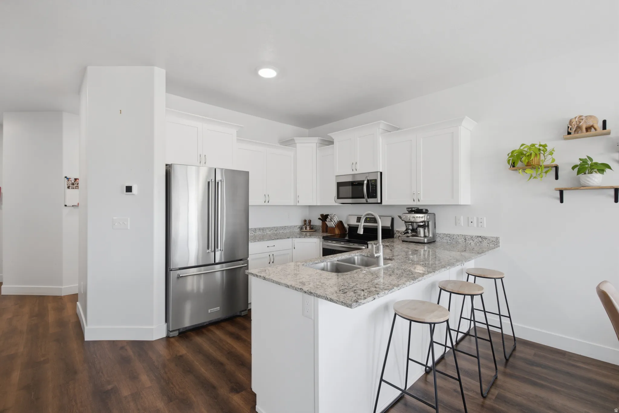 Kitchen featuring white cabinetry, stainless steel appliances, a double basin sink, light-colored granite countertops, and wood-finish flooring