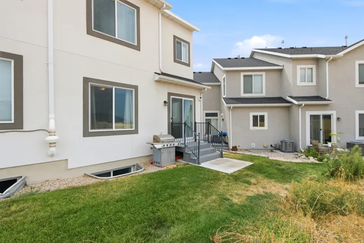 Stucco exterior with contrasting trim, multiple window installations, ground-level access, and a concrete patio with stairs