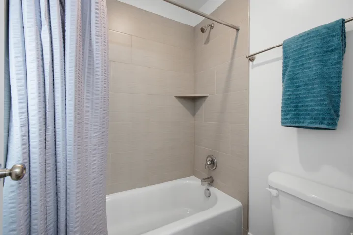 Bathtub with an integrated shower, tiled surround with a corner shelf, and brushed nickel fixtures