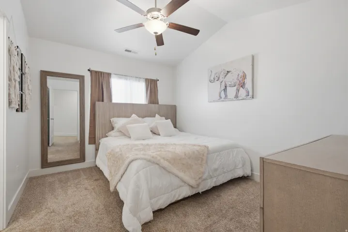 Vaulted ceiling with a ceiling fan, light wood-finish headboard, window with drapes, and neutral carpeting