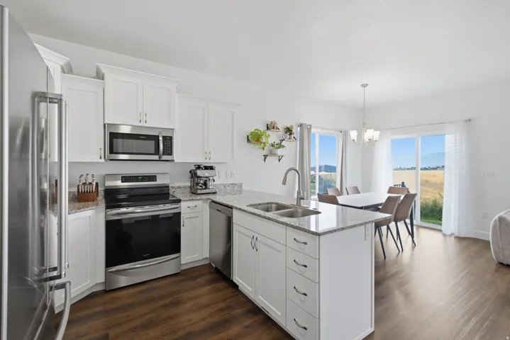Modern kitchen featuring white cabinetry, granite countertops, stainless steel appliances, wood-finish flooring, and a kitchen island with a double sink