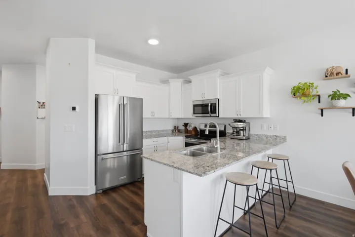 Kitchen featuring white cabinetry, stainless steel appliances, a double basin sink, light-colored granite countertops, and wood-finish flooring