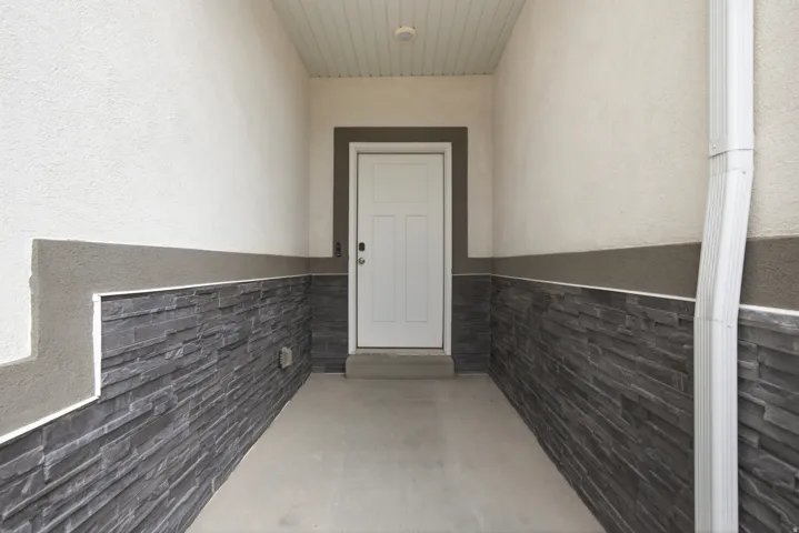 Entryway featuring white stucco, stacked stone wainscoting, and a white paneled door