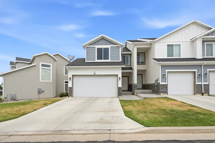 Modern townhome exterior featuring an attached garage, concrete driveway, and stone facade accents