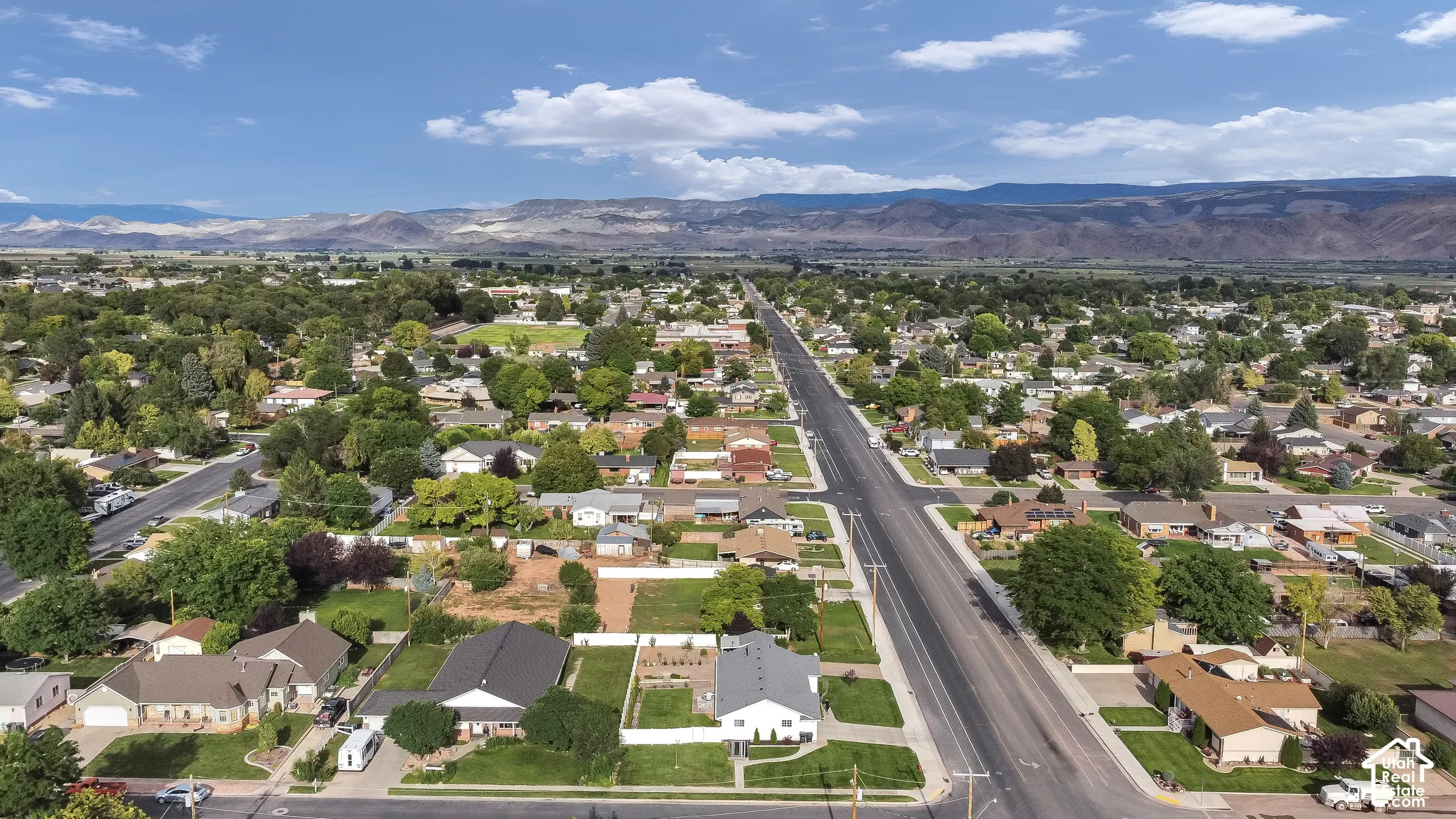 Aerial perspective of a residential neighborhood featuring mature trees, paved streets, and distant mountain ranges