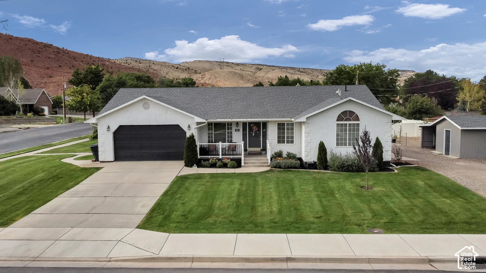 White exterior with a dark shingle roof, attached garage, front porch, and landscaped front yard