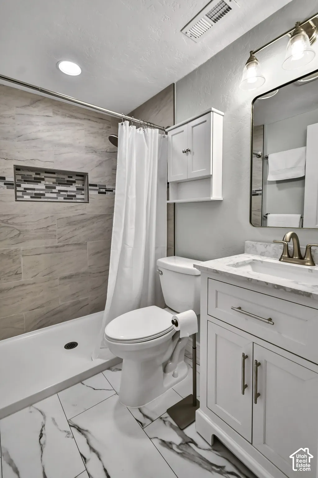 Bathroom featuring a walk-in shower with tiled surround and integrated niche, white vanity with stone-look countertop, rectangular undermount sink, and recessed ceiling lighting