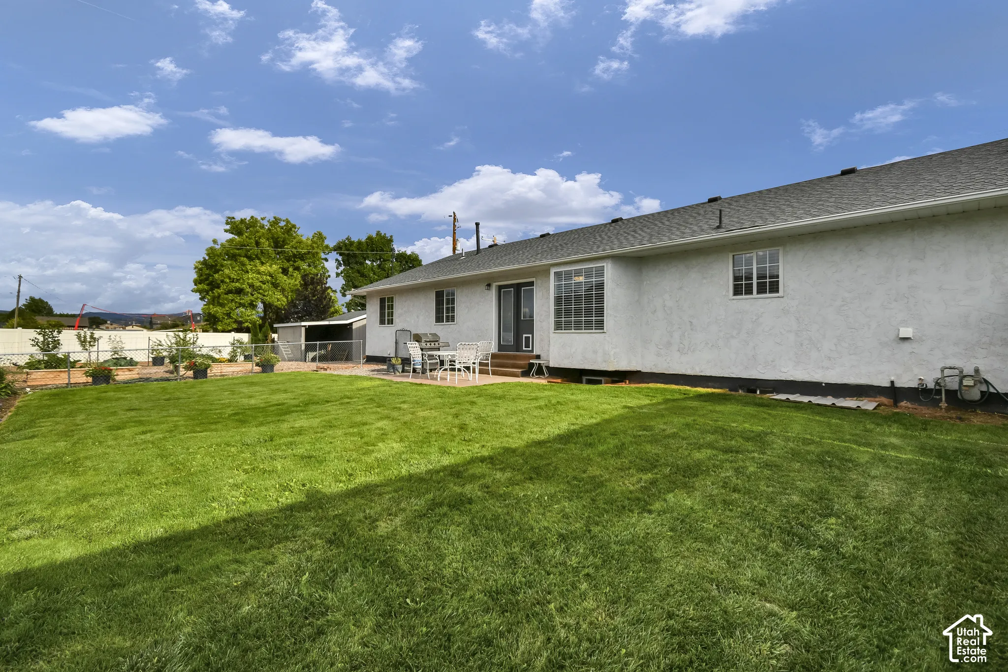 Expansive green lawn, stucco exterior, rear patio, bay window, and a utility shed