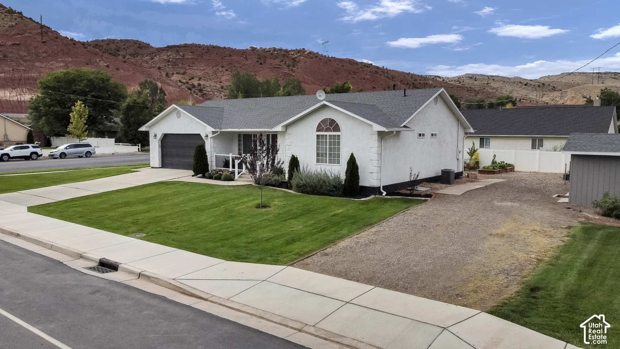 White stucco exterior, dark shingled roof, attached garage with dark door, arched window detail, and gravel side yard