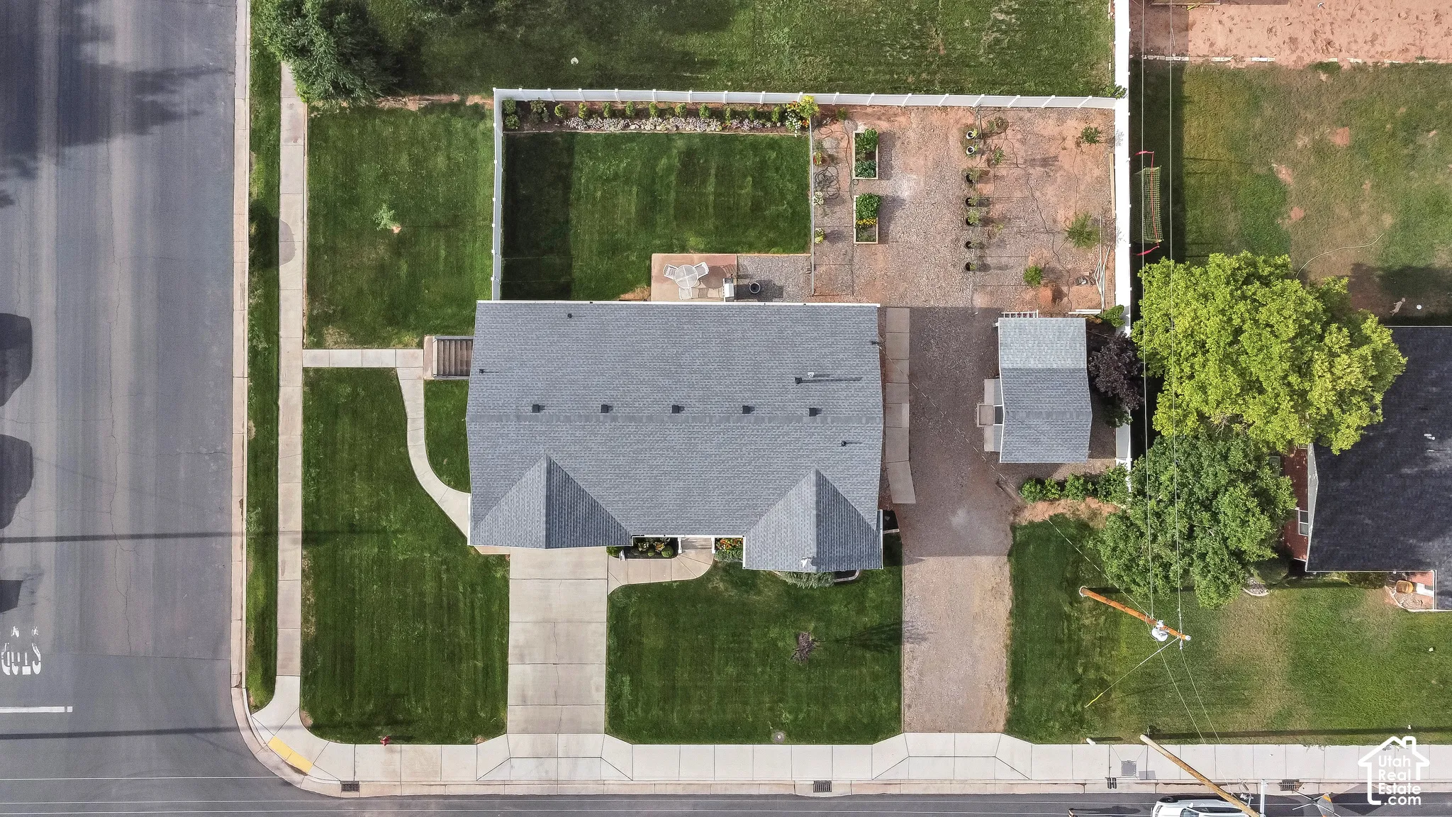 Gable roofline, front lawn with concrete walkway and driveway, gravel side yard, fenced backyard with lawn, and an outbuilding with a gable roof