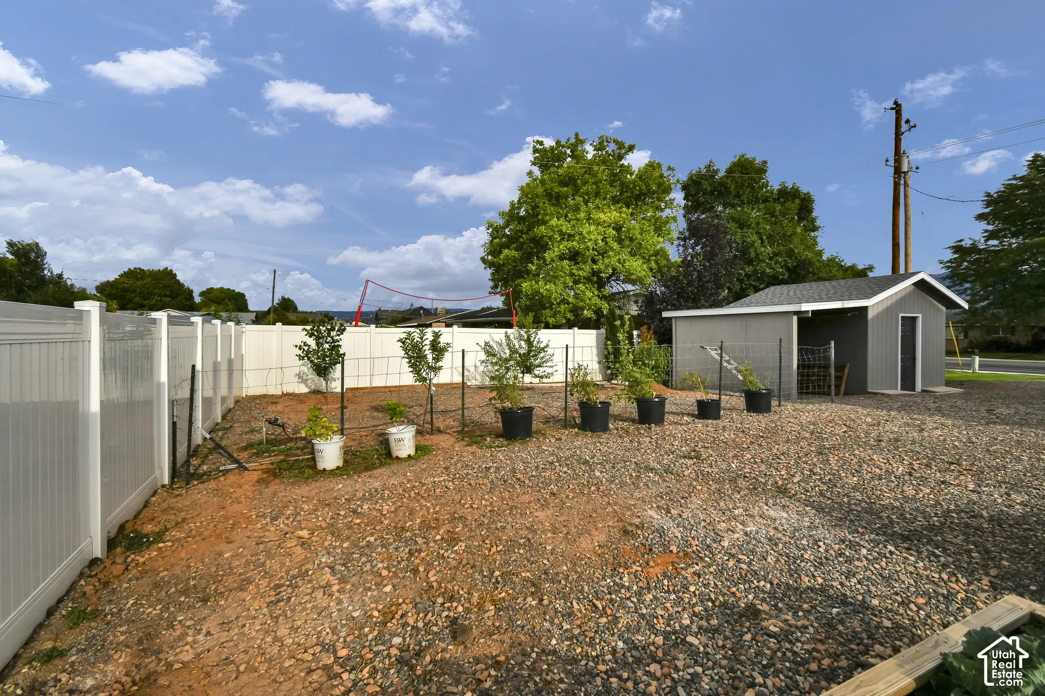 Gravel yard with a white privacy fence, a detached shed with a gray exterior, and established trees