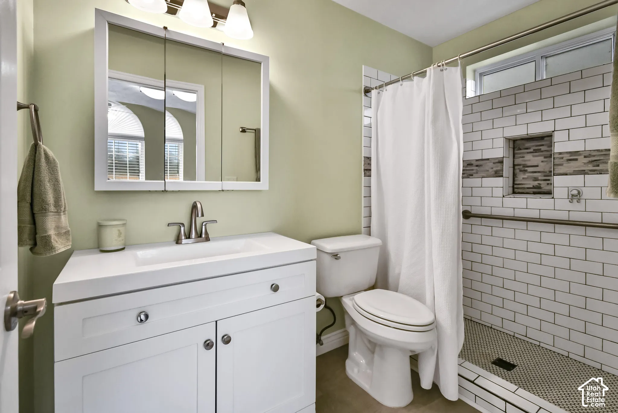 White vanity with integrated sink, subway tile shower surround, mosaic tile shower niche, and mosaic tile shower floor
