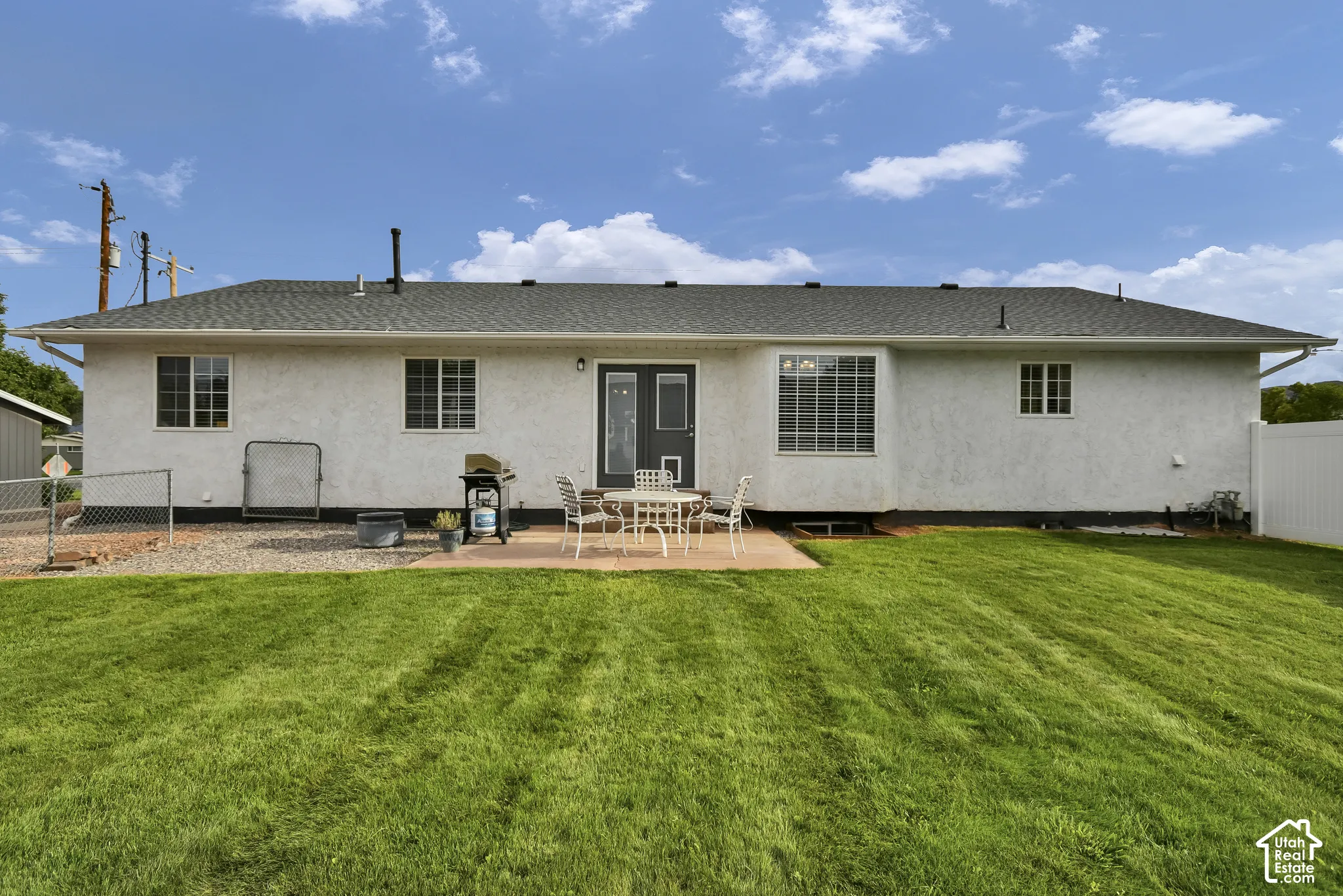 Expansive green lawn, concrete patio, white stucco exterior, multiple windows, and a privacy fence