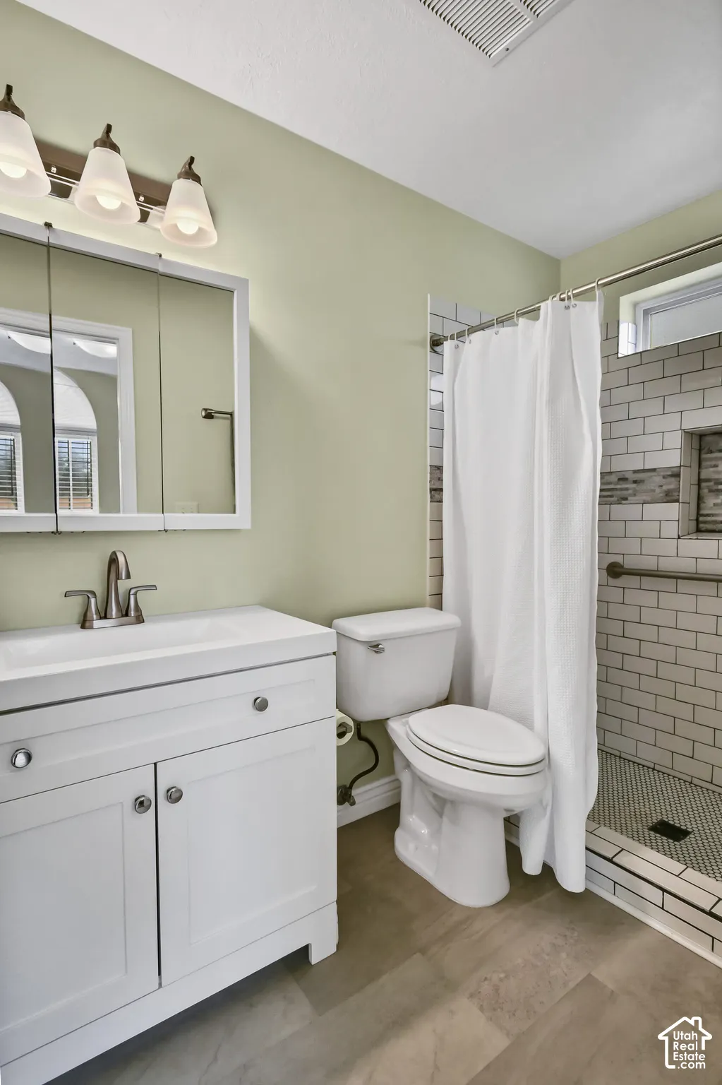 White vanity with integrated sink and brushed nickel faucet, tiled walk-in shower with grab bar, built-in shower shelf, and mosaic tile flooring