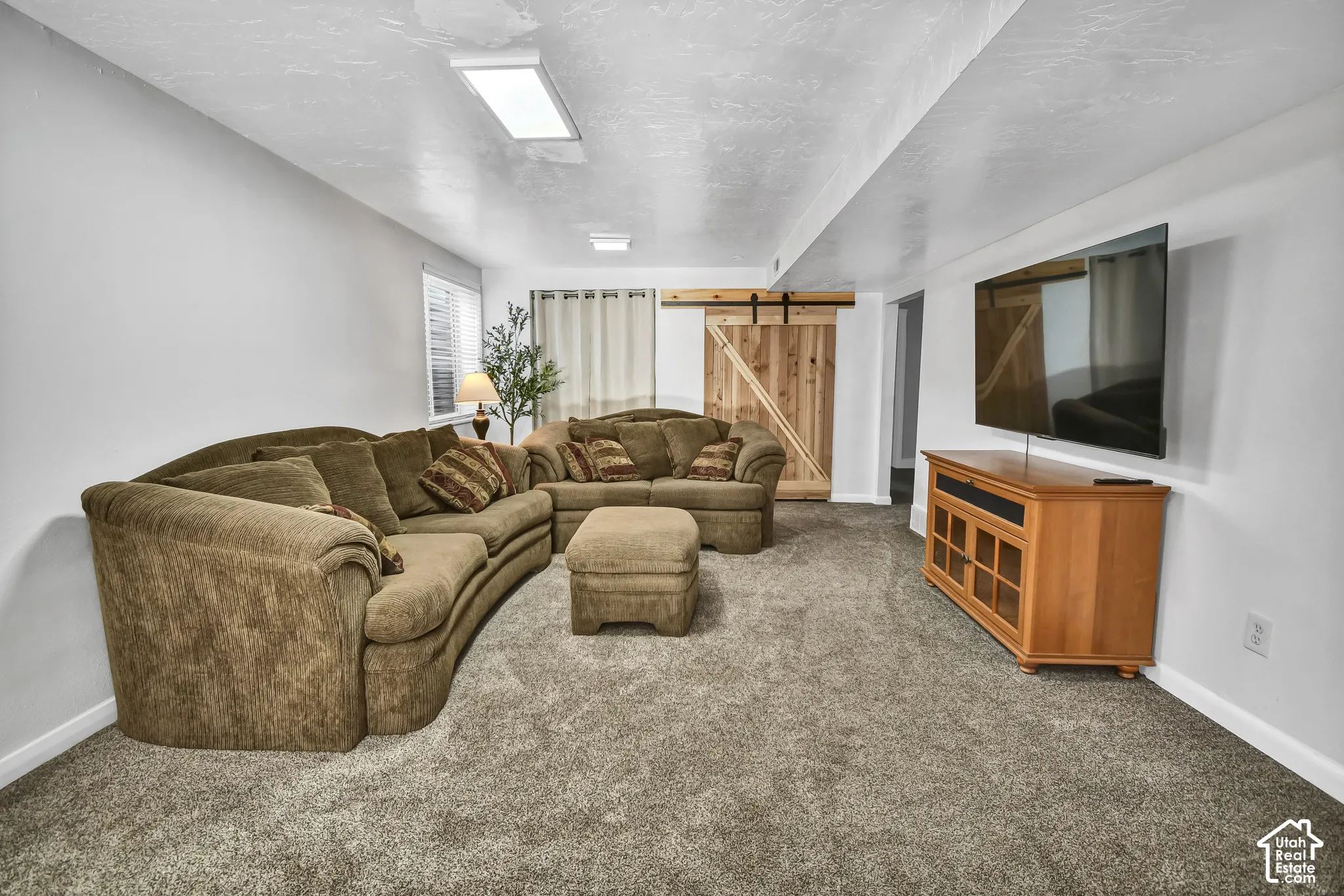Carpeted living area featuring white walls, recessed lighting, and a barn door