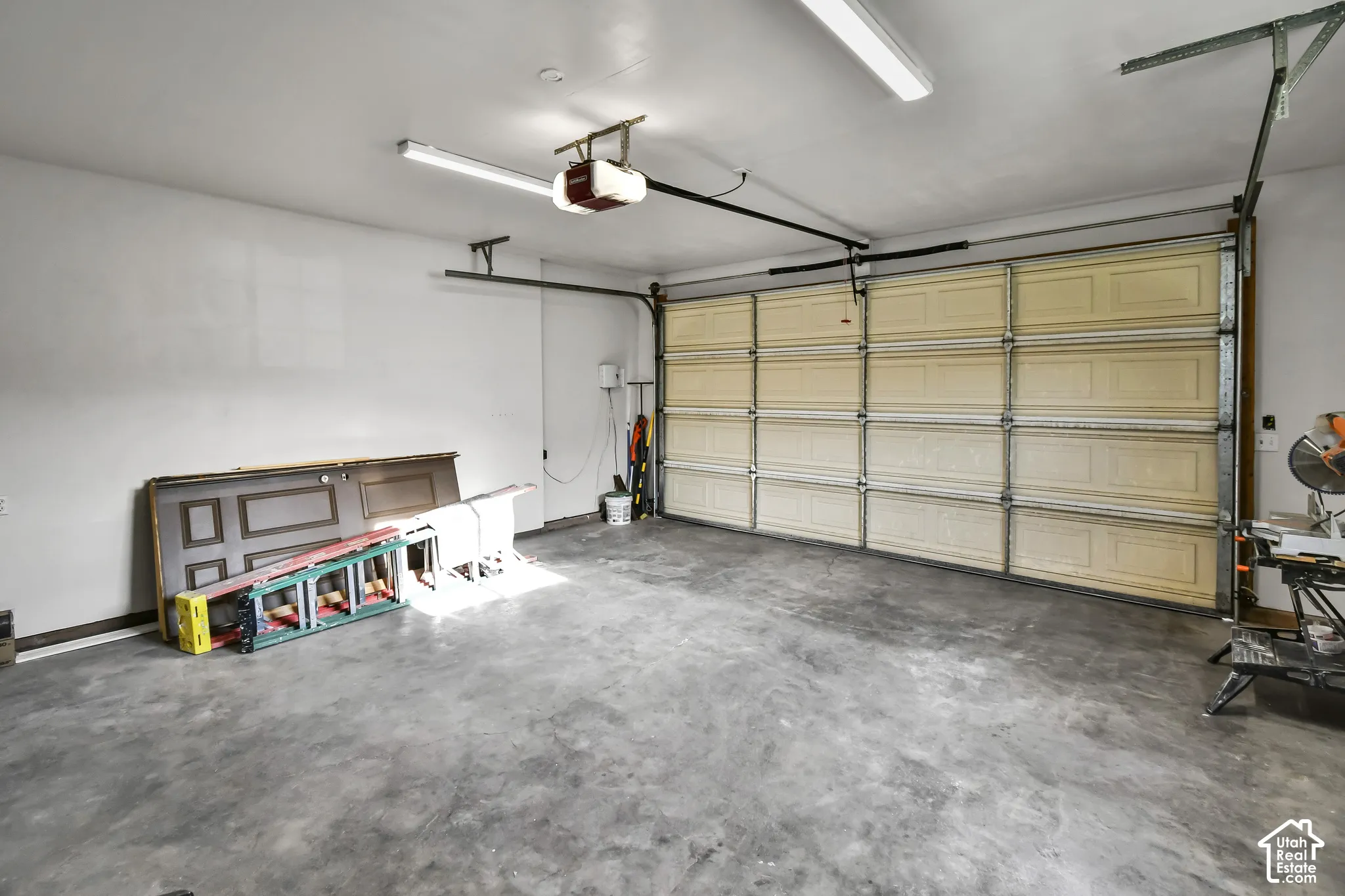 Concrete flooring, white walls, overhead lighting, garage door, garage door opener