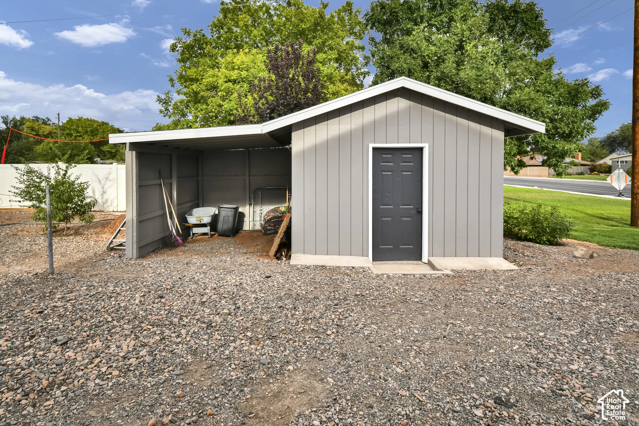 Modern storage structure featuring a metal-frame design with a spacious covered carport area, single entry door with dark finish, and gravel foundation