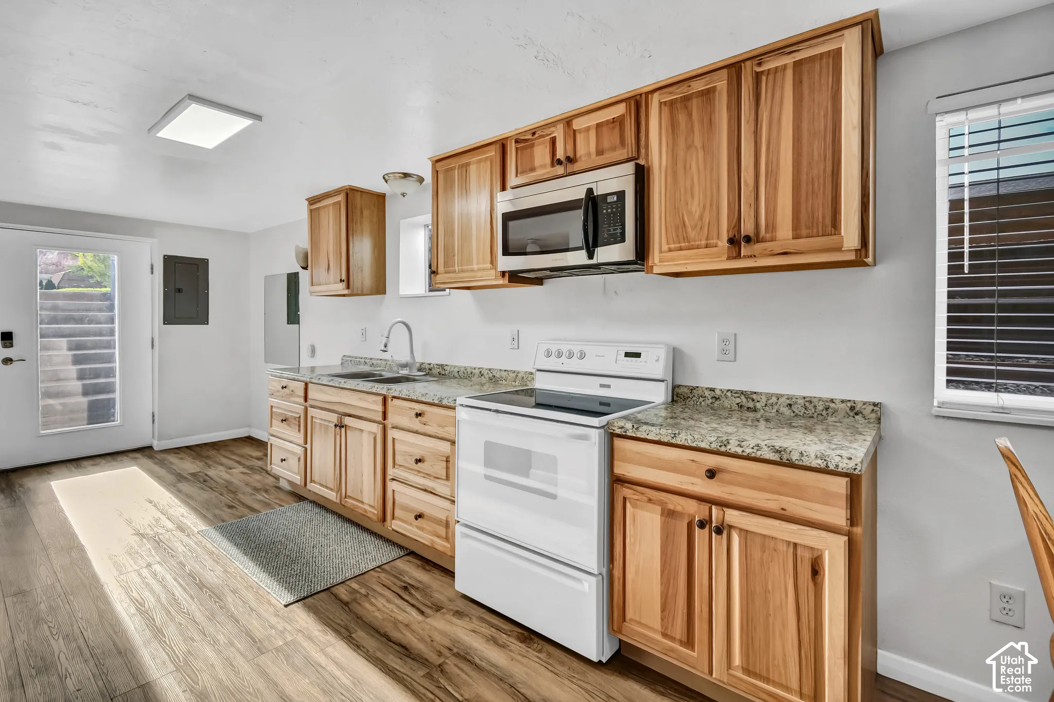 Kitchen with wood-finish flooring, natural wood cabinetry, light-toned countertops, and a full suite of appliances