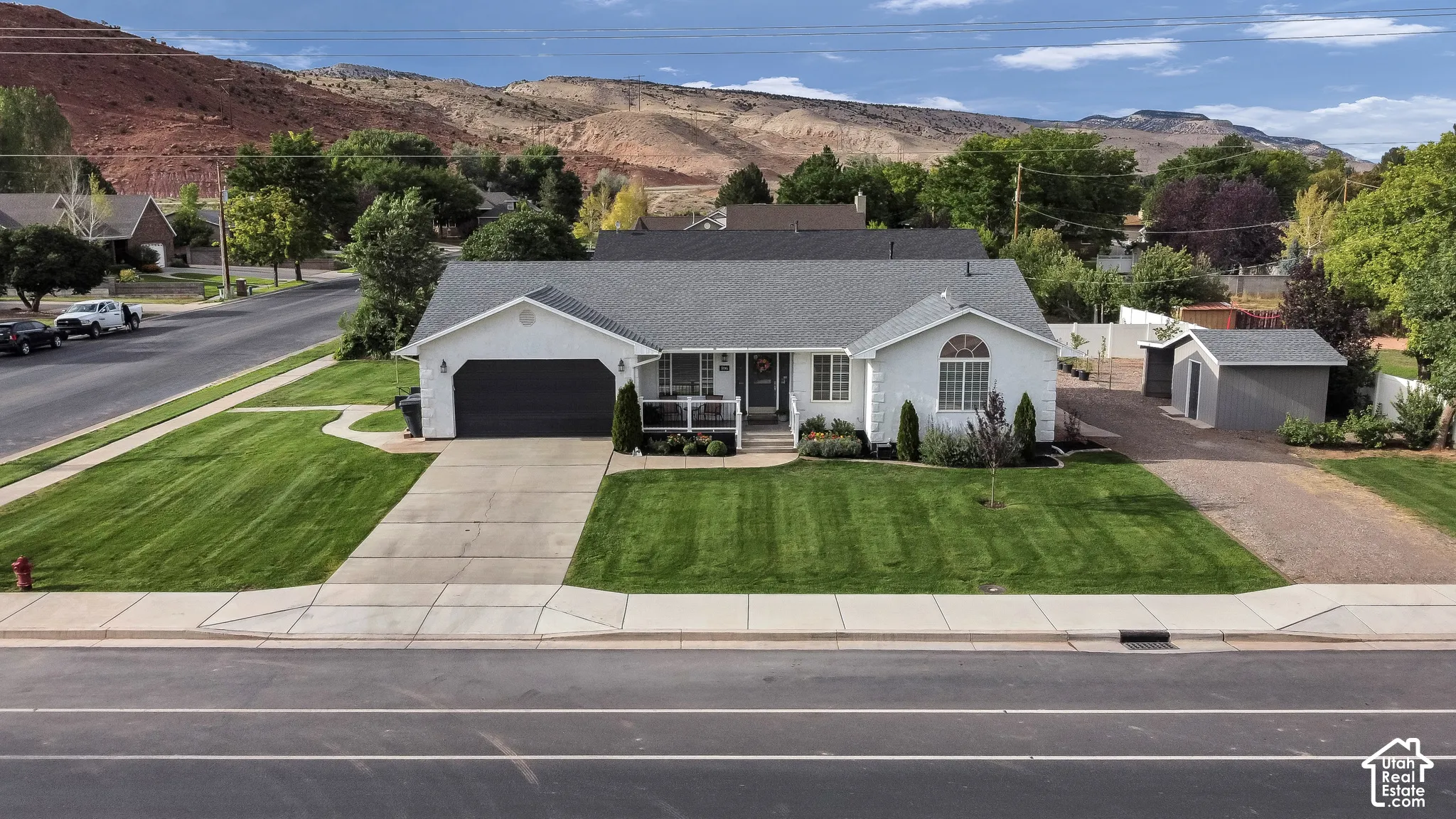 White siding exterior with a dark gray shingle roof, attached garage with a dark gray door, concrete driveway, and a gravel side parking area