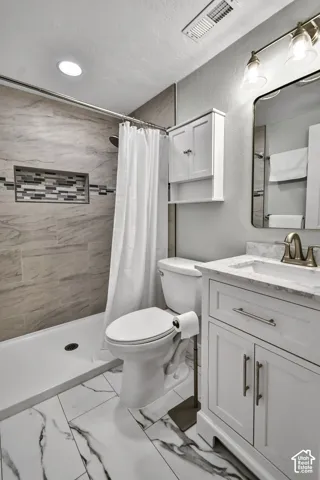 Bathroom featuring a walk-in shower with tiled surround and integrated niche, white vanity with stone-look countertop, rectangular undermount sink, and recessed ceiling lighting