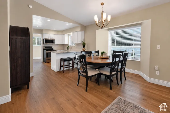 Open-concept kitchen and dining area featuring wood-finish flooring, white cabinetry, stainless steel appliances, and a counter-height island with seating
