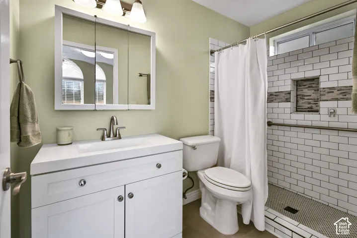 White vanity with integrated sink, subway tile shower surround, mosaic tile shower niche, and mosaic tile shower floor