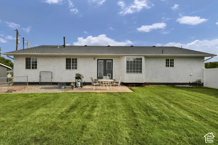 Expansive green lawn, concrete patio, white stucco exterior, multiple windows, and a privacy fence