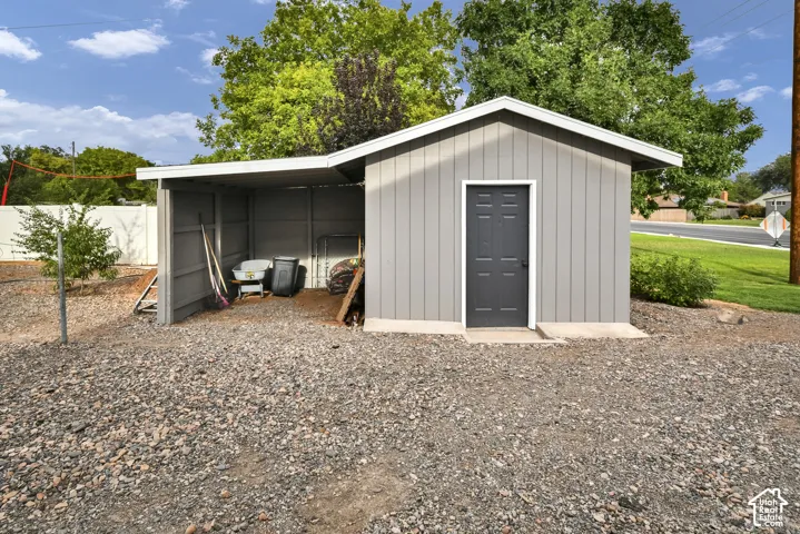 Modern storage structure featuring a metal-frame design with a spacious covered carport area, single entry door with dark finish, and gravel foundation