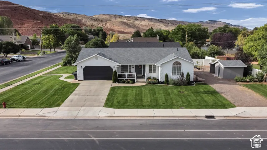 White siding exterior with a dark gray shingle roof, attached garage with a dark gray door, concrete driveway, and a gravel side parking area