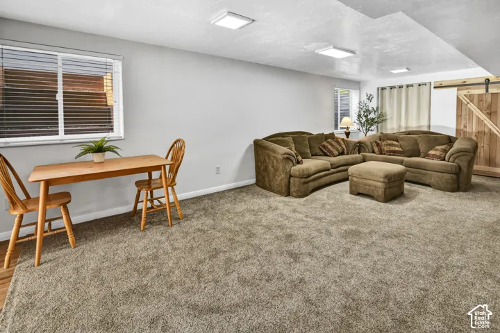 Plush carpet flooring, recessed ceiling lighting, a wood-finish barn door, and white window blinds