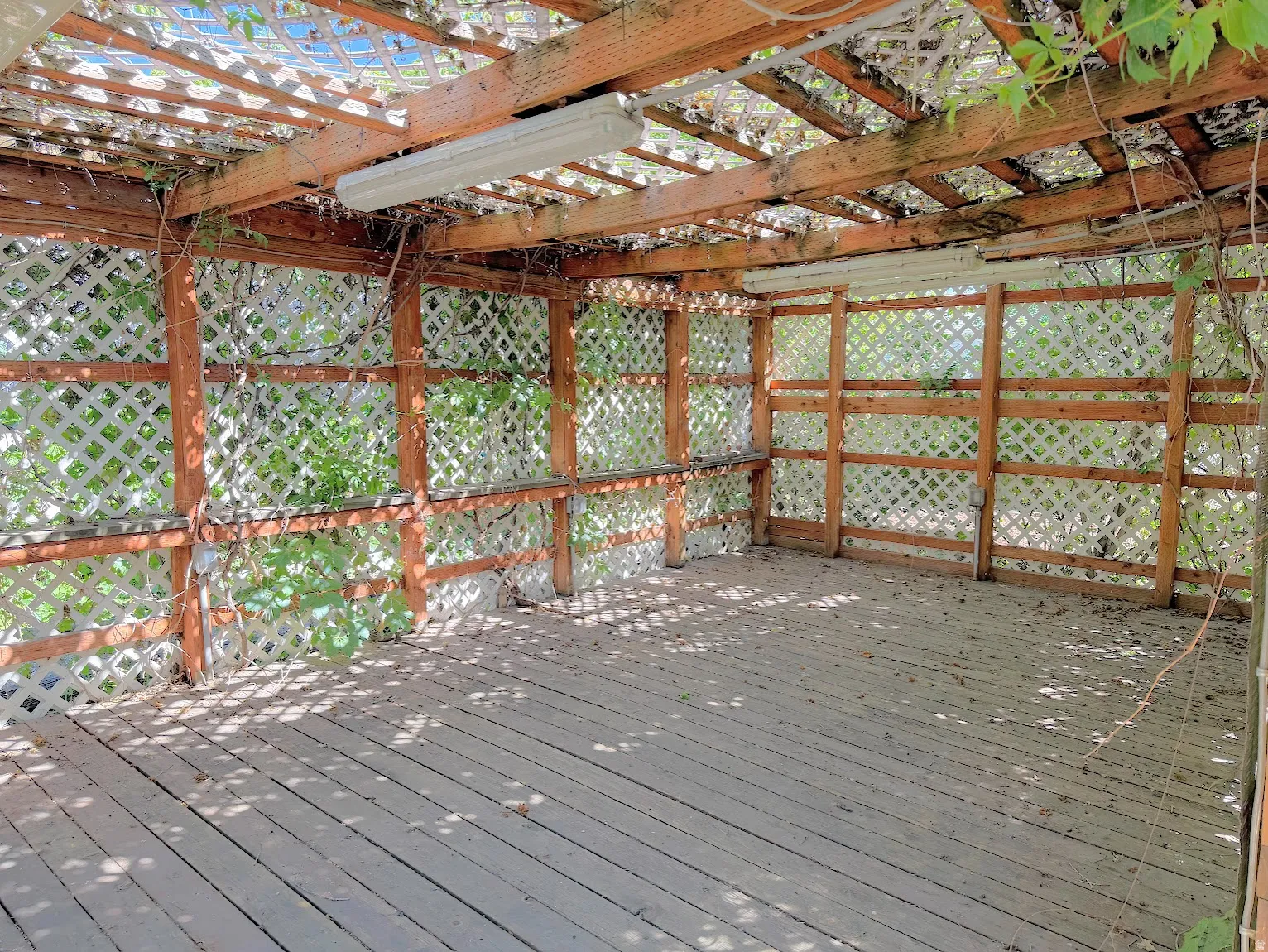 Covered outdoor space featuring a wood-plank deck, lattice walls, wood beam ceiling, and overhead lighting